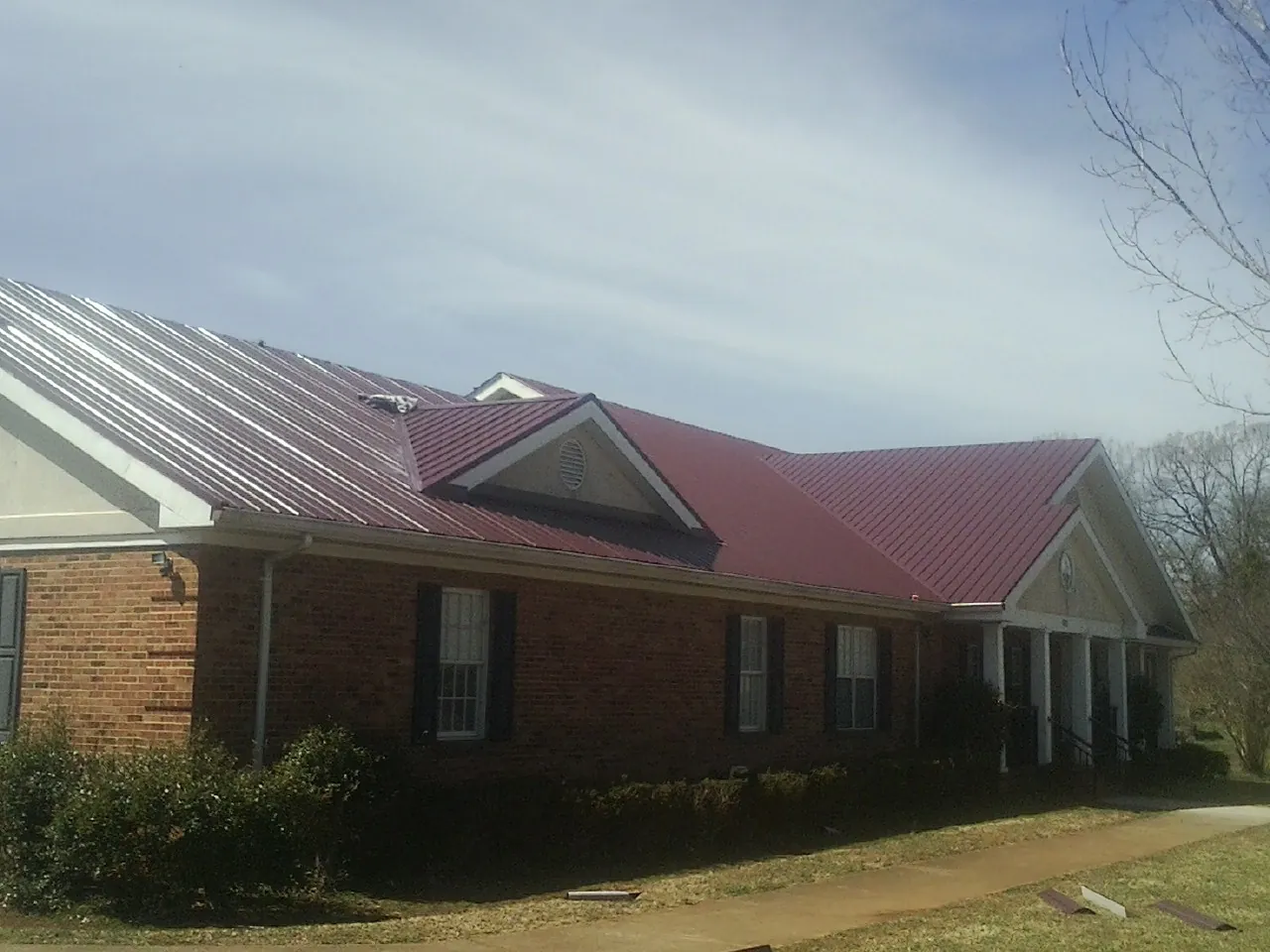Red metal roof with gabled entries on a long brick building, from a Hail Damage Roof Repair job in Zebulon