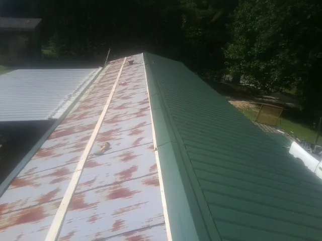 Old rusted panels beside newly installed green metal roofing — Wind Damage Roof Repair by Roofing Brothers in Zebulon