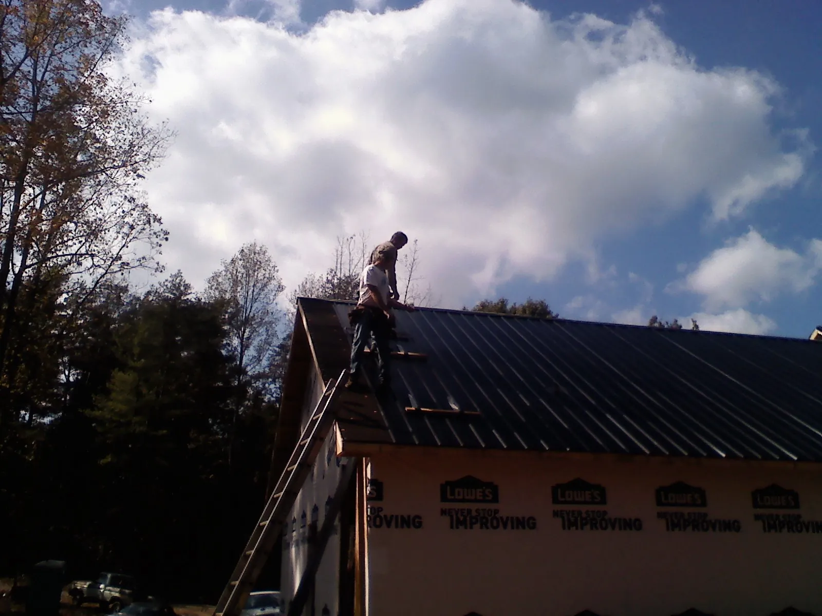 Roofer fastening dark metal panels high against a cloudy sky, from a Roof Inspection job in Zebulon